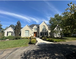 A luxurious stone home in Indian Hill, Ohio, with a newly installed Charcoal Timberline HDZ roof. The house features a manicured lawn, a curved driveway, and elegant architectural details under a bright blue sky.