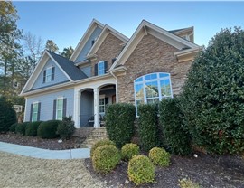 A stylish home in Holly Springs, NC, featuring a newly installed Pewter Gray Timberline GAF shingle roof, stone and shingle siding, white trim, and black shutters, surrounded by neatly maintained landscaping.