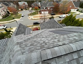 Close-up view of a Pewter Gray GAF Solar Shingles roof installation in Cary, NC, showcasing integrated solar technology with a uniform shingle design, overlooking a suburban neighborhood with brick homes and tree-lined streets.