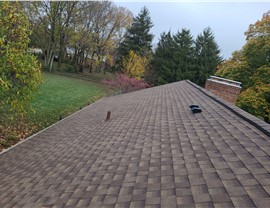 New roof installation in Fairfield, Ohio, using Barkwood Timberline HDZ shingles from GAF, surrounded by trees with autumn leaves and a brick chimney in the background.