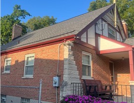 Brick home in Blue Ash, Ohio, with a new roof featuring Williamsburg Slate shingles from GAF, a landscaped flower bed with purple flowers, and a front porch with outdoor seating.