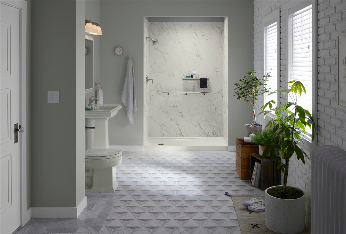 Spacious sage green bathroom featuring a Reveal by KOHLER walk-in shower with Crosscut Dune LuxStone walls, a pedestal sink, toilet, geometric grey floor tile, and large indoor plants by a shuttered window