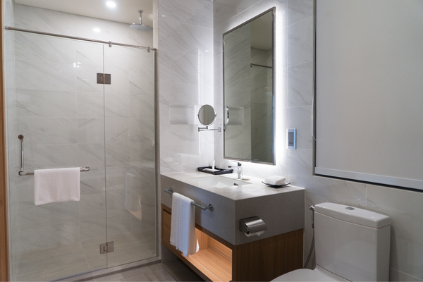 Modern primary bathroom featuring a walk-in shower with floor-to-ceiling grey marble tile, a vessel sink vanity with a dark wood base and marble countertop, pendant lighting, small potted plants, and a warm wood interior door with wood-look plank flooring