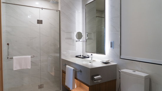 Modern primary bathroom featuring a walk-in shower with floor-to-ceiling grey marble tile, a vessel sink vanity with a dark wood base and marble countertop, pendant lighting, small potted plants, and a warm wood interior door with wood-look plank flooring