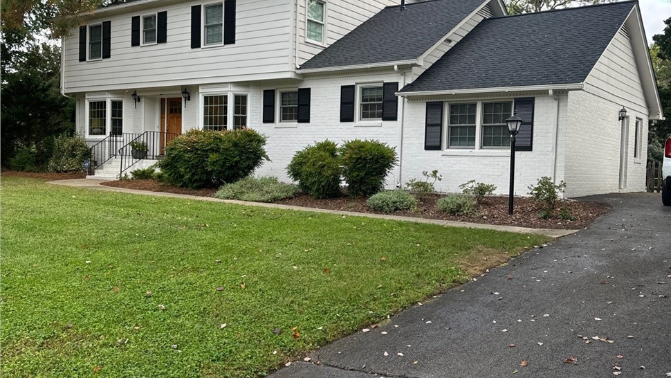 Two-story white brick house with Charcoal Timberline HDZ shingles, black shutters, a wood-stained front door, and a well-maintained lawn, located in Henrico, VA.