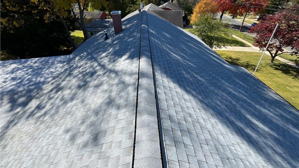 Newly installed Fox Hollow Gray Timberline HDZ roof in Rockville, MD, with a clear ridge line and surrounded by autumn trees and suburban homes.