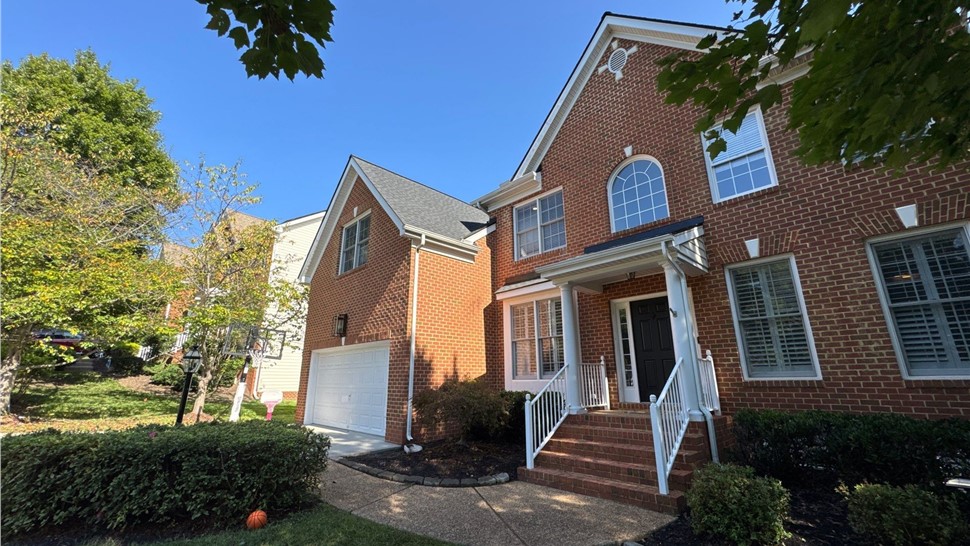 A two-story brick house with Charcoal Timberline HDZ shingles installed on the roof, featuring white trim, a black front door, and a landscaped lawn under a clear blue sky in Midlothian, VA.