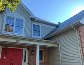 Close-up of a two-story home in Reston, VA, with a new roof replacement using Pewter Gray Timberline HDZ shingles, light-colored siding, and red double front doors under a sunny, blue sky.