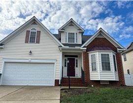 Front view of a house in Henrico, Virginia, with a newly installed Pewter Gray Timberline HDZ shingle roof. The home features white siding, brick accents, a maroon roof trim, and a white garage door under a partly cloudy blue sky.