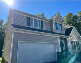 Front view of a two-story house in Henrico, Virginia, with a newly installed roof featuring Slate Gray Timberline HDZ shingles. The home has beige siding, green shutters, and a white garage door under a bright blue sky.