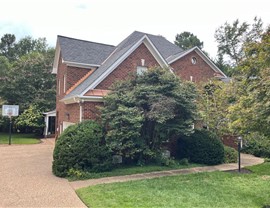 A two-story brick house with Antique Slate Camelot II shingles, copper accent roof, lush greenery, and a basketball hoop in the driveway under an overcast sky in Midlothian, VA.