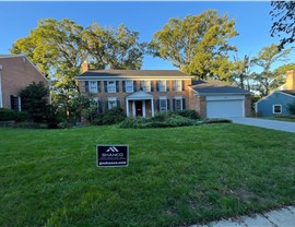 Two-story light brick home in Alexandria, VA, featuring black shutters and white-trimmed windows. The roof showcases newly installed Royal Sovereign Charcoal shingles, complementing the home's classic design.