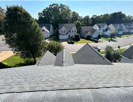 A rooftop view of a Pewter Gray Timberline HDZ shingle installation in Henrico, VA, overlooking a suburban neighborhood with houses, trees, and a quiet street.