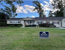 Cream-colored ranch home with green shutters in Fairfax, VA, showcasing a newly installed roof with Barkwood Timberline HDZ shingles. The property features a spacious front yard and neatly manicured shrubs as part of the landscaping.
