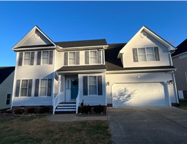 Two-story white home in Chesterfield, VA, with a newly replaced Charcoal Timberline HDZ shingle roof, gray shutters, a teal front door, and a two-car garage, set against a bright blue sky.