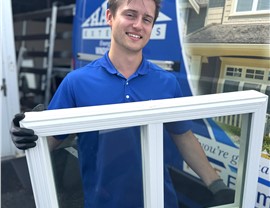 Harley Exteriors window installer holding a sample of the window he's about the install while standing in front of the company vehicle. 