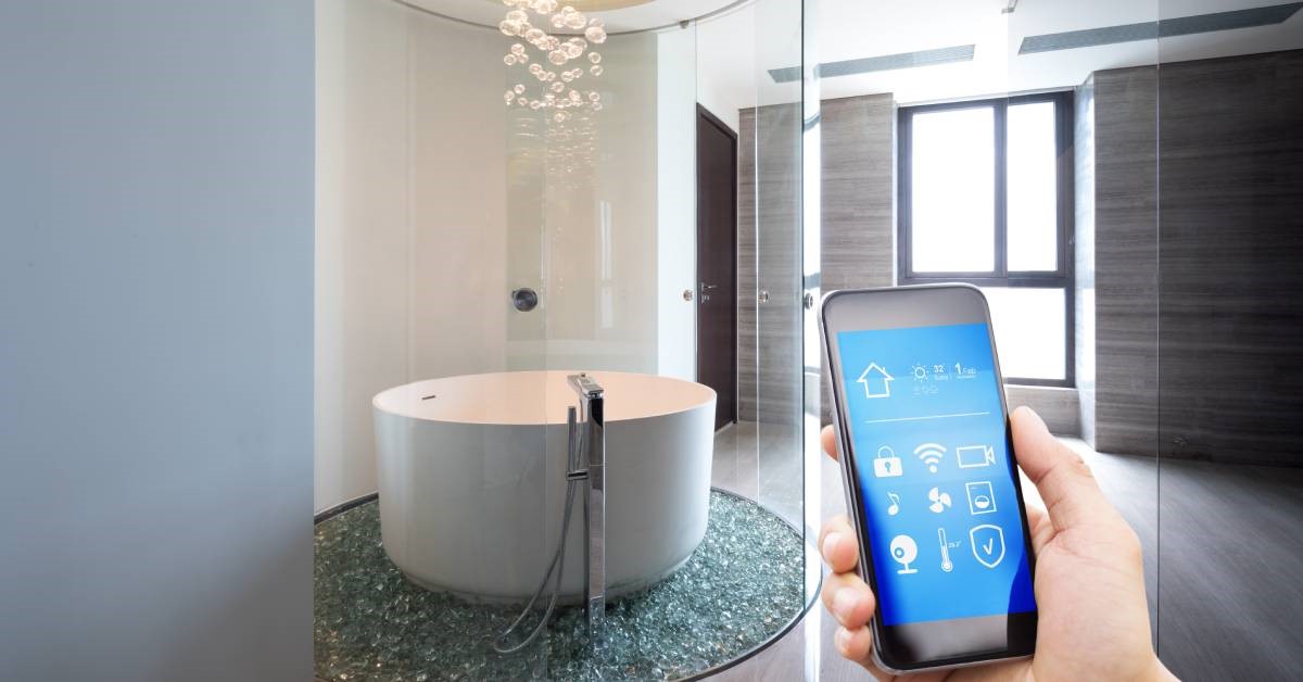 A person’s hand holding their smartphone, using an application to adjust various settings in their smart and modern bathroom.