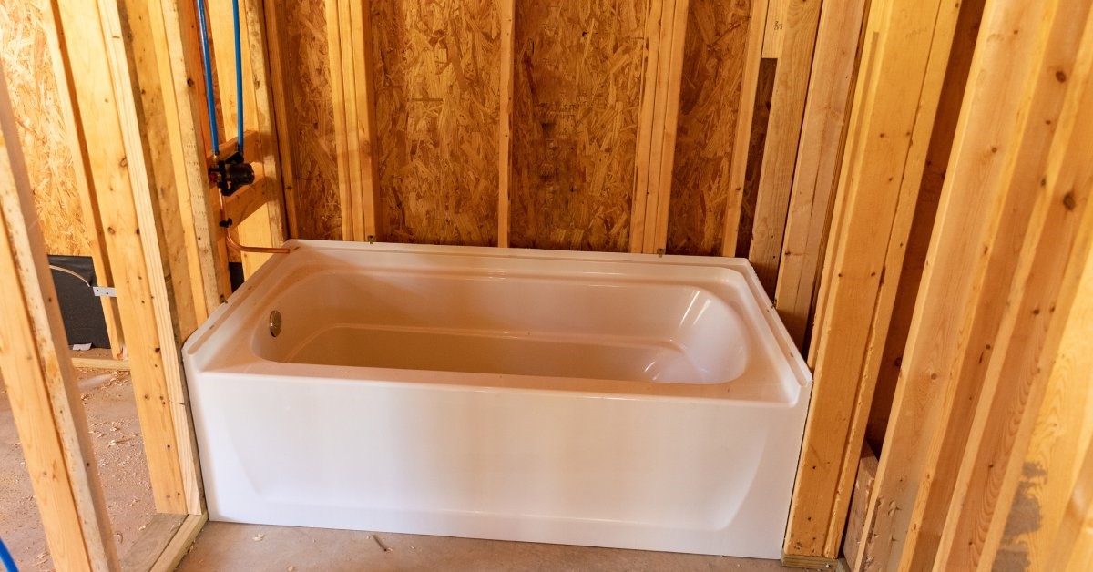 A residential bathroom in the early stages of building. There is a bathtub surrounded by framed-in walls.