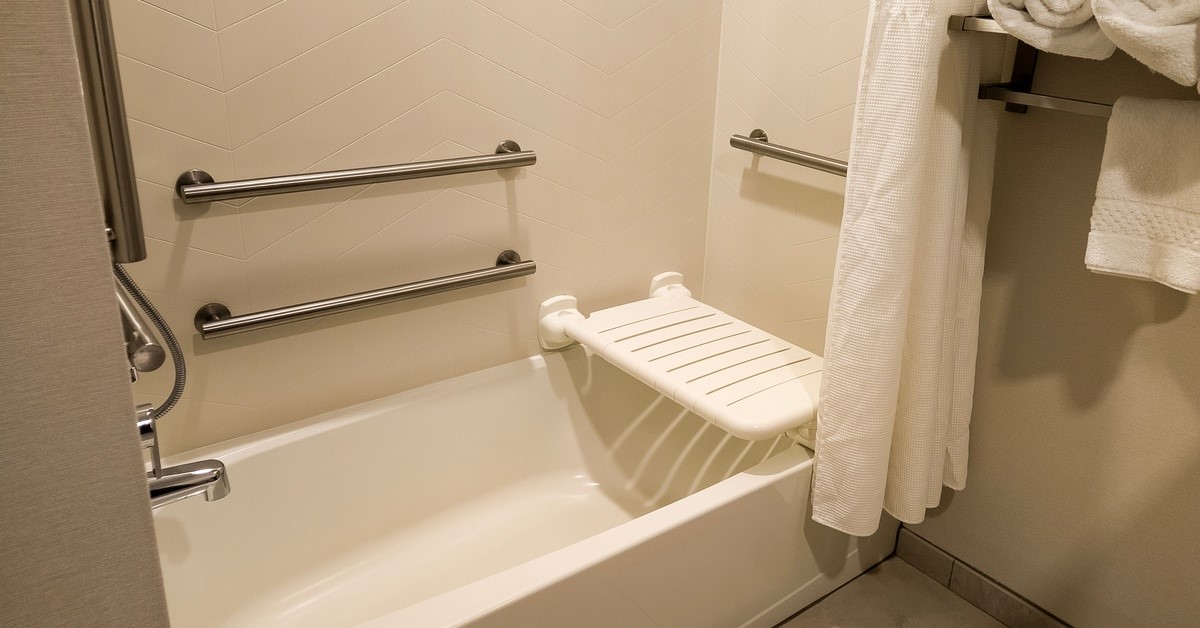 A traditional bathtub with several towels on a shelf next to the tub. There is a white plastic seat installed above the tub.