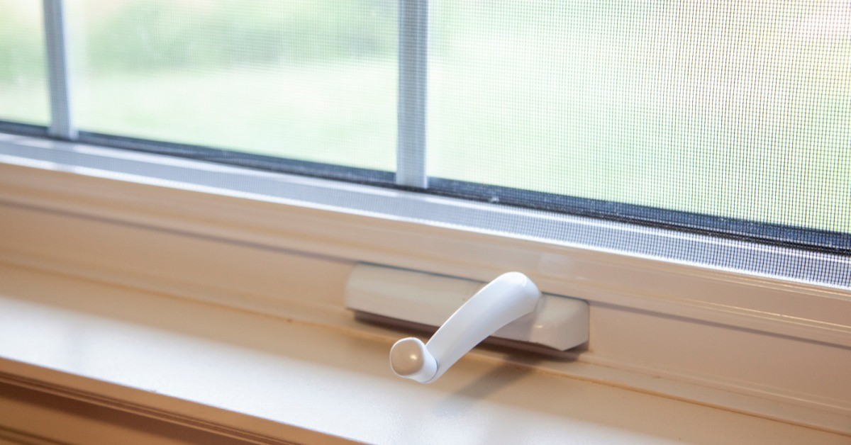 A hand crank to a window is sitting on a windowsill. The glass of the window is in the background.