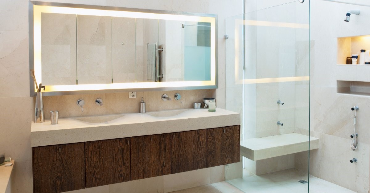 A modern home bathroom featuring a double vanity, large mirror, and glass-enclosed shower with a bench and multiple showerheads.