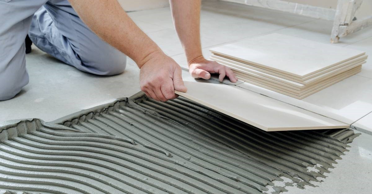 A professional contractor carefully laying large ceramic tiles on tile adhesive as part of his bathroom remodel.