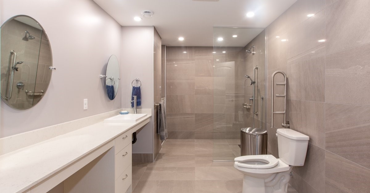 A modern and well-lit accessible bathroom, featuring a zero-threshold roll-in shower and wall-mounted grab bars.