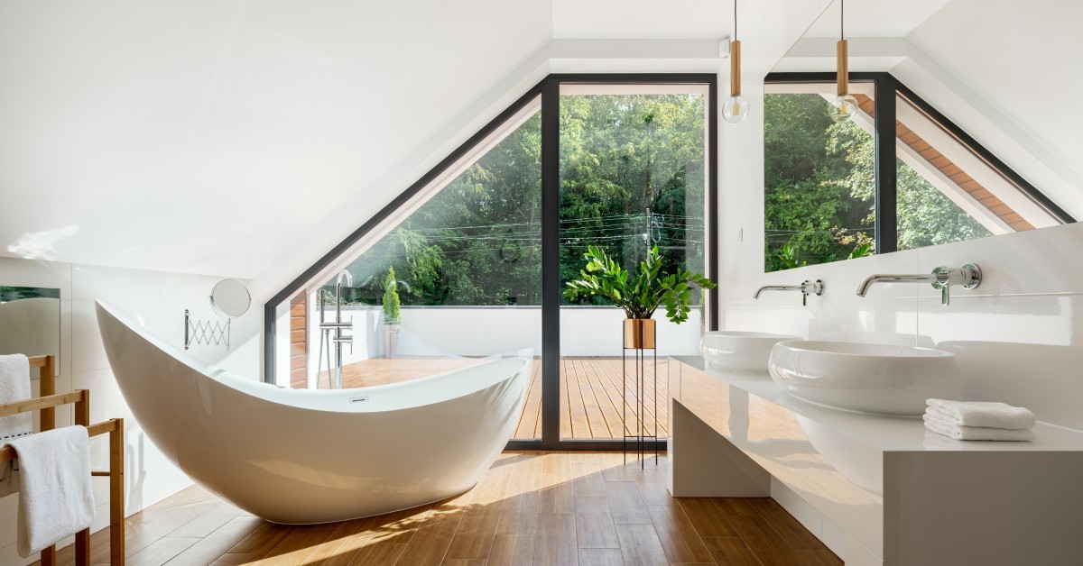 A bathroom with a tub to the left of frame and a sink to the right. There is a large window along the far wall.
