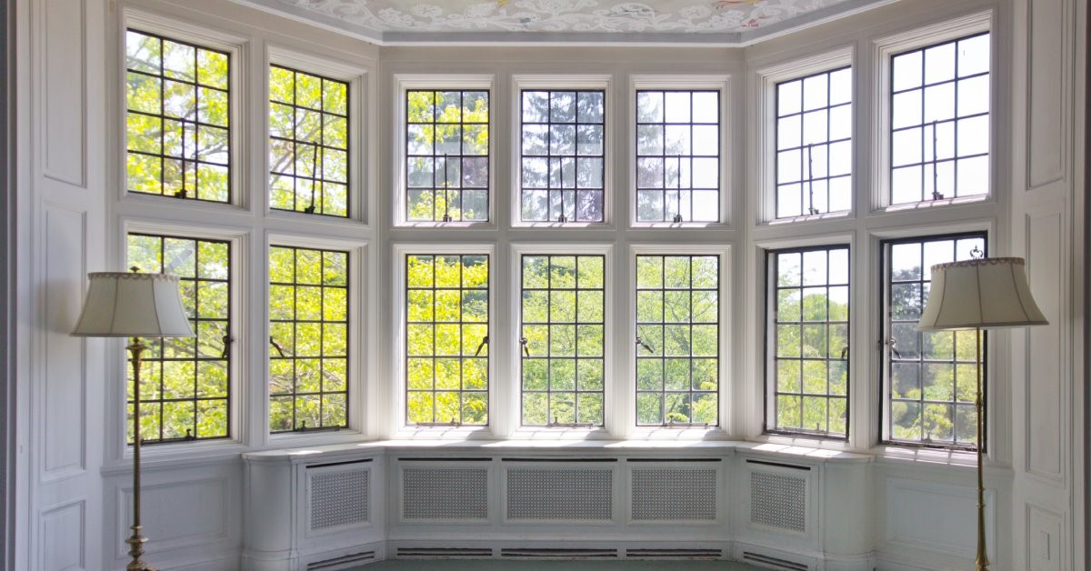 Large, classic, French-pane bay windows under a decorative, hand-painted ceiling inside a nearly empty home.