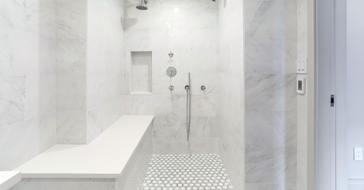 A shower with a marble design. There is a bench to the left and a door to the right of the frame.