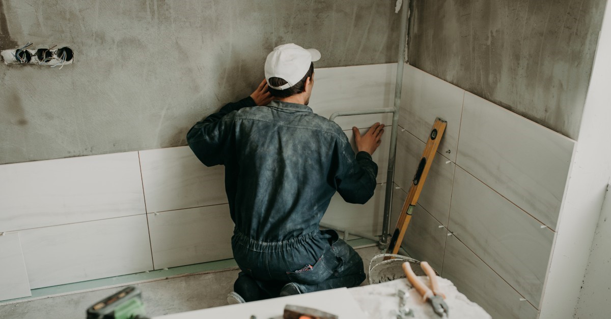 A professional contractor placing modern glass and ceramic shower tiles on the walls of his client’s future shower.