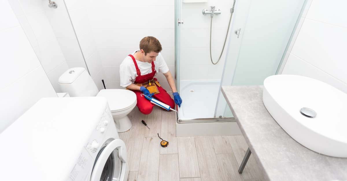 A professional contractor using a caulk gun to seal the shower pan on his client’s tub-to-shower conversion.