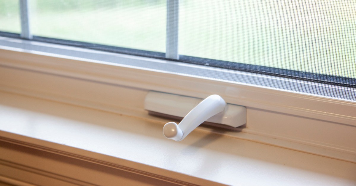 A hand crank to a window is sitting on top of a windowsill. There is a window behind the crank.