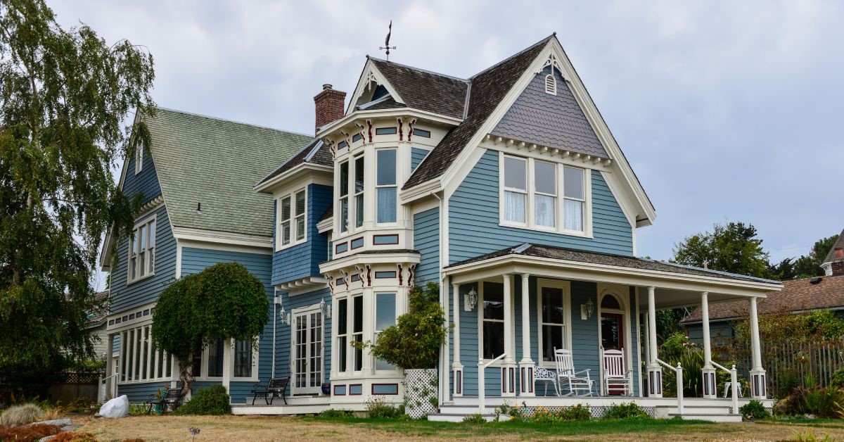 A Victorian-style historic home, painted blue with clean white wooden accents, and full of large windows.