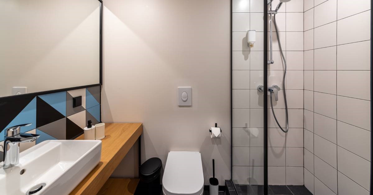 A recently renovated residential home bathroom featuring a well-installed tub-to-shower conversion and a colorful backsplash.