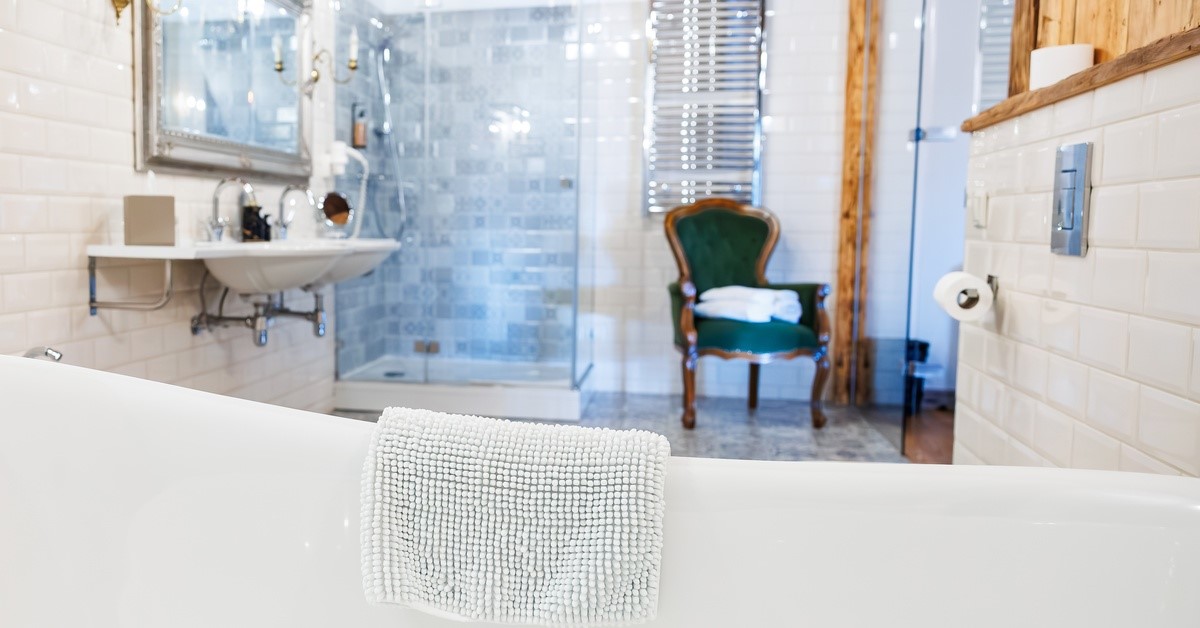 A bathroom with a chair to the right of frame and a sink to the left. There is a shower in the background.