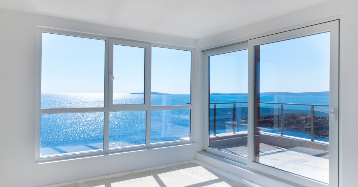The corner of a room with several windows on the walls. The windows lookout to a body of water.