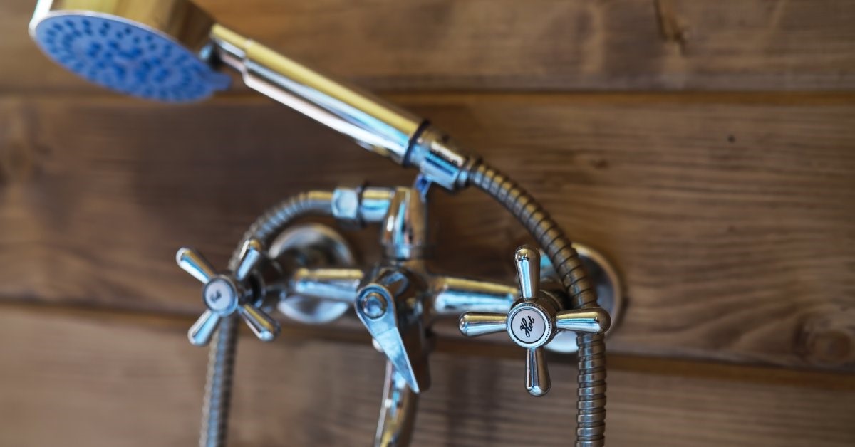 A close-up view of an adjustable metal showerhead attached to hot and cold valves on a wood paneled wall.