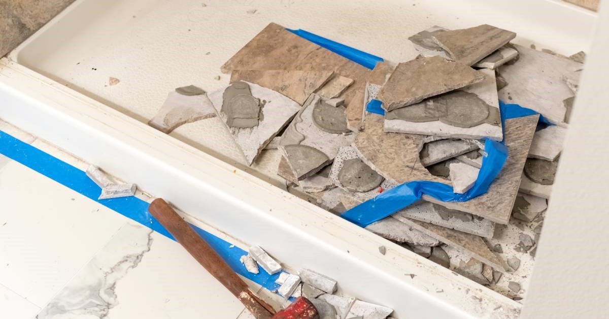 A pile of demolished bathroom tiles lies in the shallow tub of a shower, indicating a tub-to-shower conversion project.