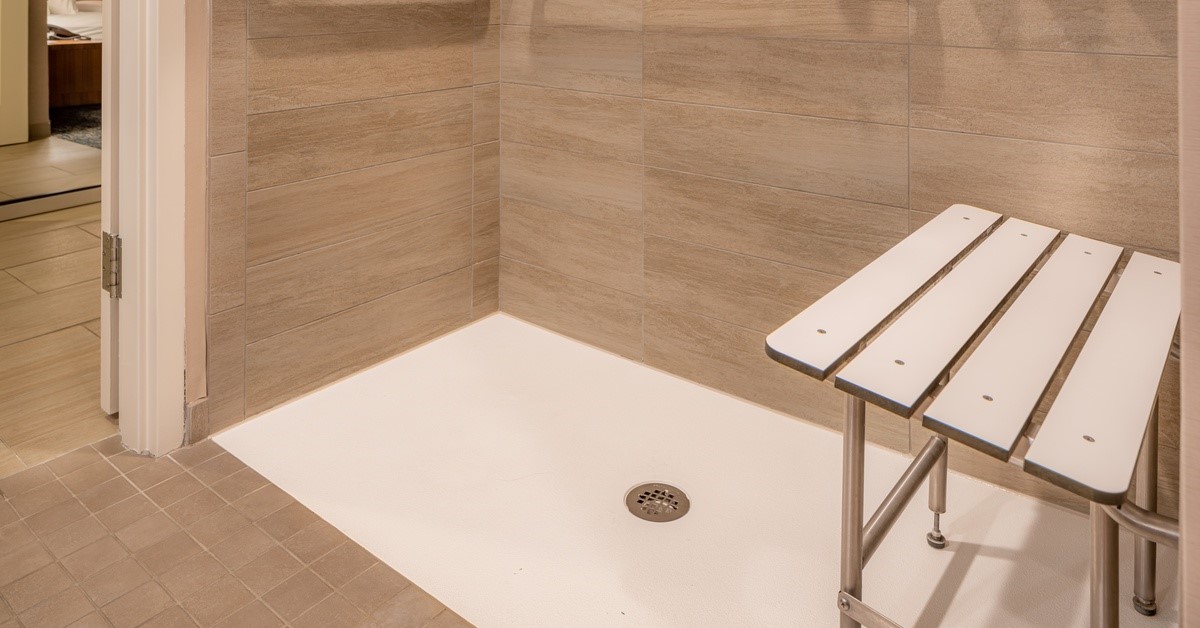 An accessible roll-in shower that has two safety grab bars on the wall and a bench that matches the floor.
