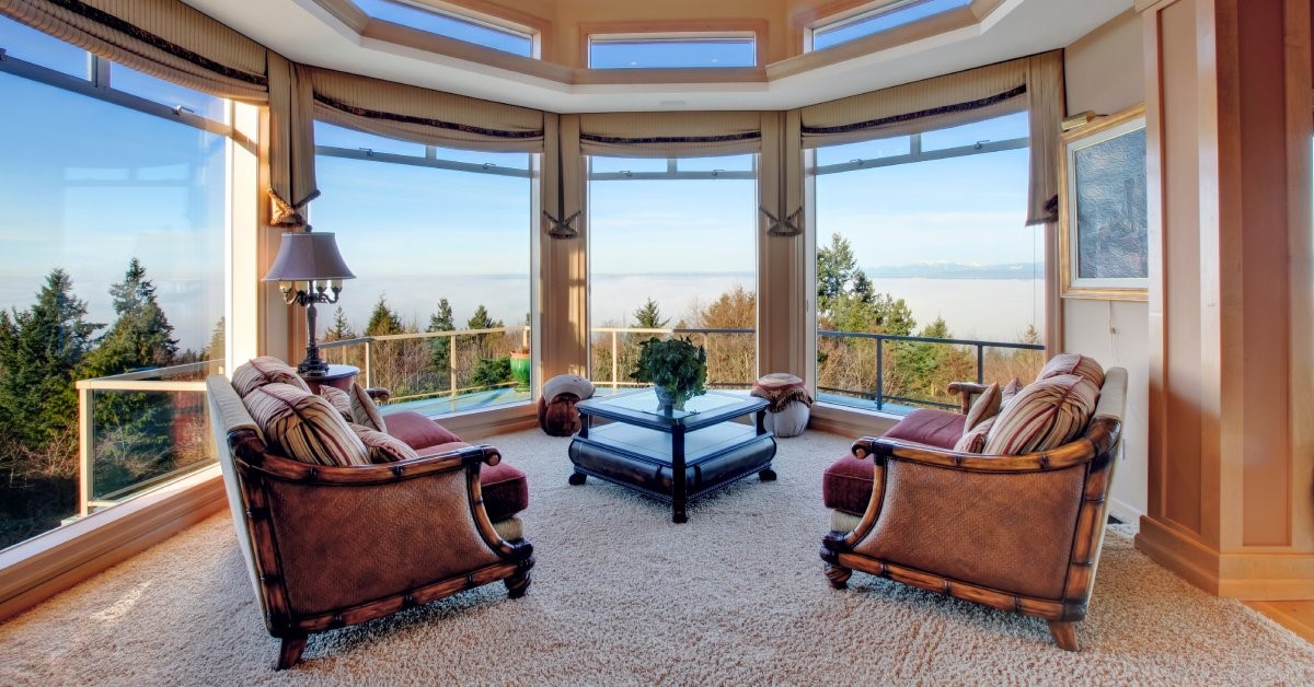 A large and luxurious sunroom, boasting four large picture windows overlooking mountainous, forested terrain.