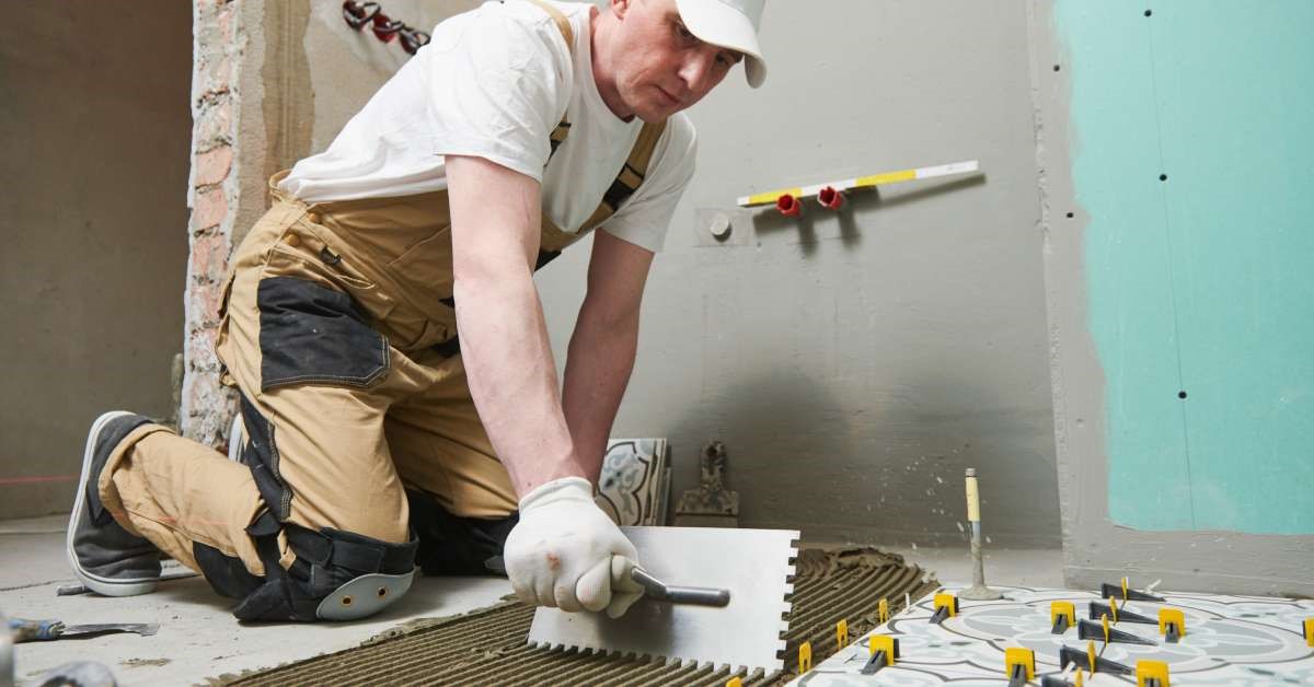 A professional contractor laying tiles in the shower as part of larger restroom renovations for his client.