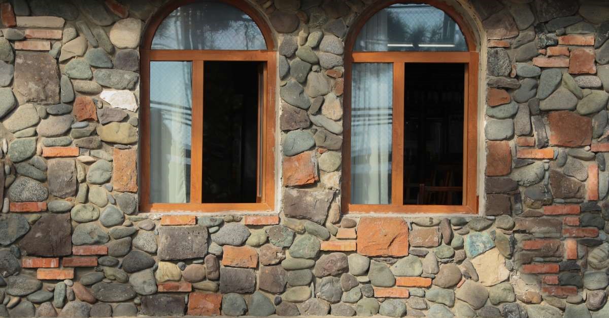 An old cobblestone and brick home with recently renovated wooden window frames. The two windows are open.