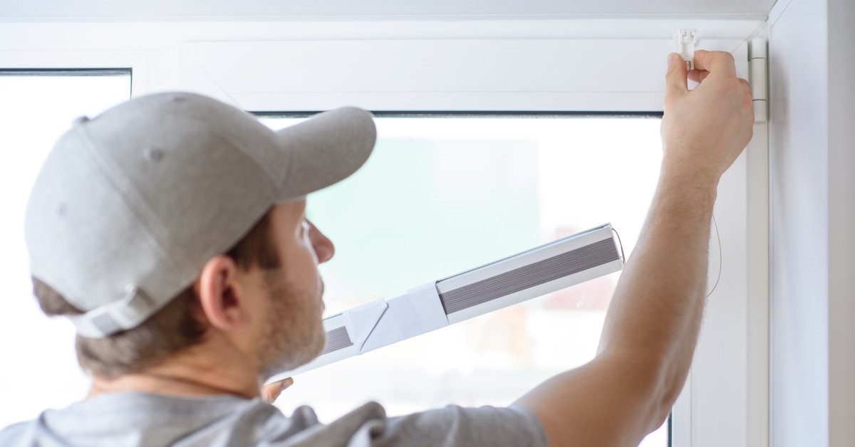 A professional contractor measuring his client’s windows and installing pleated blinds—a common window treatment.