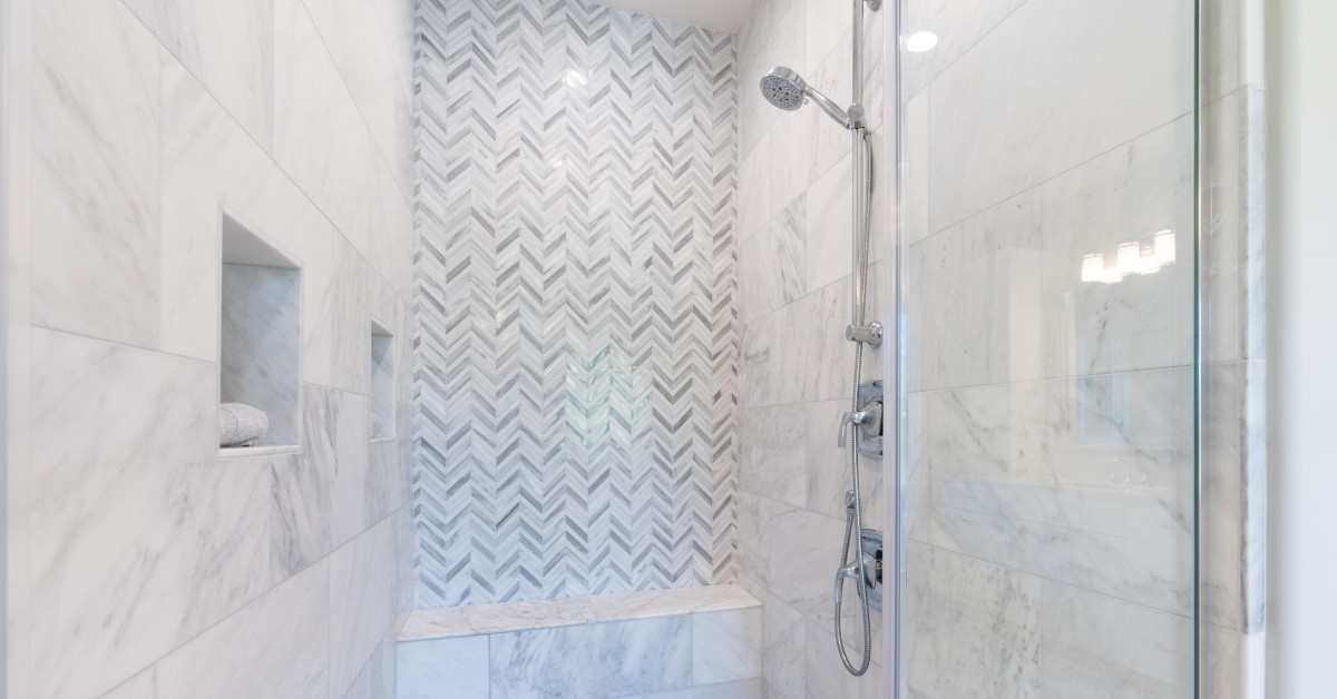 Walk-in shower with white and gray pattern tile, overhead rain shower, bench seating and chrome finishes.