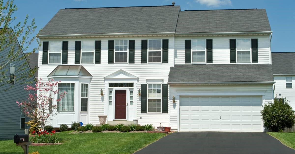 The front of a large white house. The home boasts different types of windows, including bay and sliding.