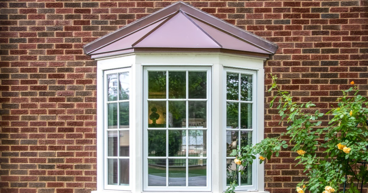 An exterior picture of a home with a window jutting out from the brick wall. The window is white.