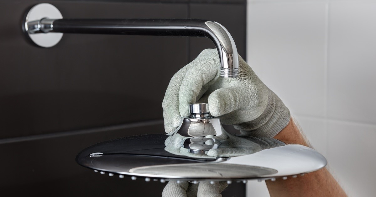 A person wearing gloves is holding onto some shower hardware. They are holding a showerhead under a pipe.
