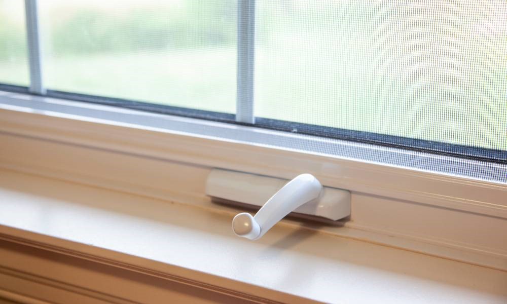 An easy-to-use white crank handle for a casement window sits just above the windowsill.