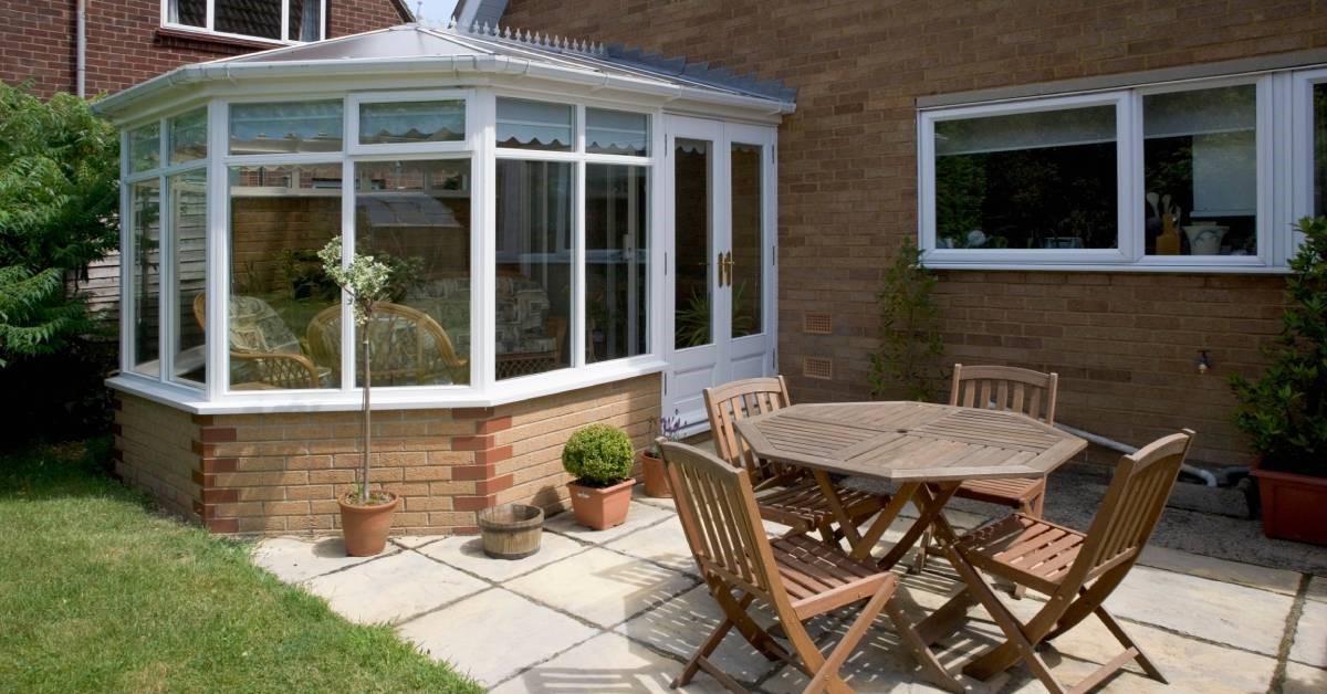 A residential home’s backyard featuring an exterior view of a sunroom with large garden windows and glass doors.